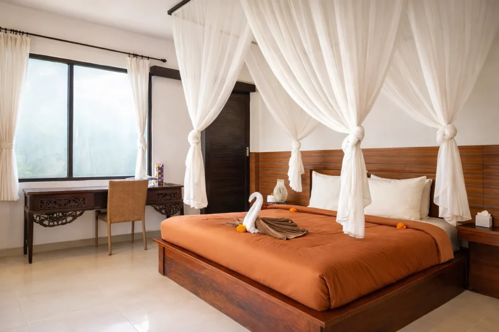 Luxurious tropical bedroom featuring a four-poster canopy bed with white drapes, orange duvet, and wooden furniture.