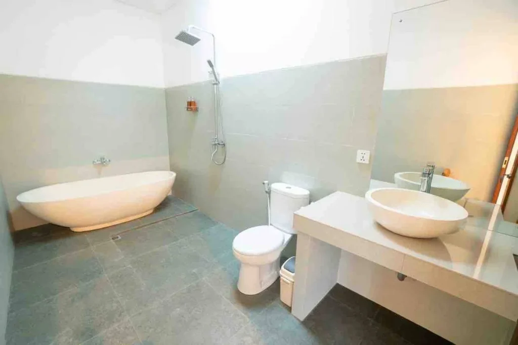 Modern minimalist bathroom featuring a sleek freestanding white bathtub, wall-mounted shower, white toilet, and a contemporary vanity with a vessel sink and large mirror.