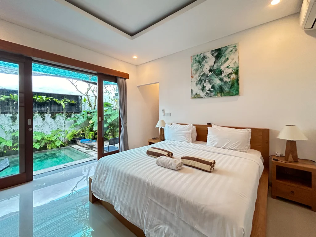 Modern bedroom with king-size bed, white linens, and direct access to a private plunge pool and lush garden through sliding glass doors.